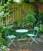 Garden chairs and table in a relaxing, serene, peaceful, lush and private home backyard in summer. Green metal patio furniture seating in an empty and tranquil courtyard with fresh flowers and plants