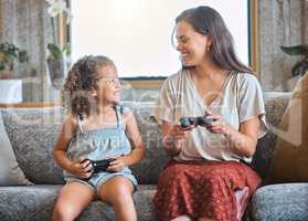 Hispanic mother and daughter playing video games together while sitting on the couch at home. Fun young mother and daughter using joysticks while playing and spending free time together on weekend