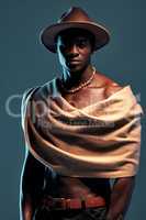 Fashionable african American model posing with wrapped scarf against blue studio background with copyspace. Sexy, serious, handsome black man with attitude wearing hat and shawl. Masculine and muscle