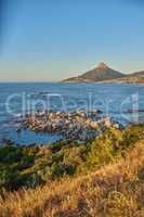 Landscape view of sea water, mountains and a blue sky with copy space of Lions Head in Cape Town, South Africa. Calm, serene and tranquil ocean and relaxing nature scenery with shrubs and brown grass
