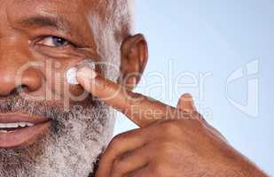 Our products has to grow with us. Studio portrait of a mature man applying moisturiser to his face against a blue background.