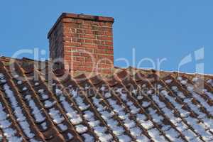 Red brick chimney designed on the roof of a snow covered residential house or building against a clear sky background. Air vent construction for the release of smoke and heat from fireplace in winter