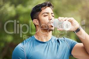 One fit young indian man taking a rest break to drink water from bottle while exercising outdoors. Male athlete quenching thirst and cooling down after running and training workout at the park