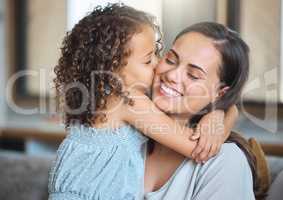 Little daughter embracing her mother from behind and gently kissing her on the cheek showing love and affection while sitting on the couch at home. Sweet moment between mother and child on mothers day