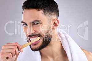 Be gentle but thorough. a young man brushing his teeth while standing against a grey background.