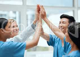 There is comfort in numbers. a group of medical practitioners joining hands to high five each other at work.