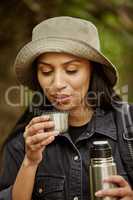 Its a little hot. an attractive young woman drinking some coffee while hiking in the wilderness.