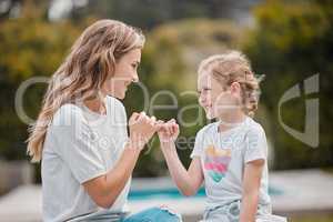 Happy young caucasian mother sitting with her adorable little daughter in the garden at home and making pinky promises. Cute little girl bonding with her parent in the backyard swearing to secrecy