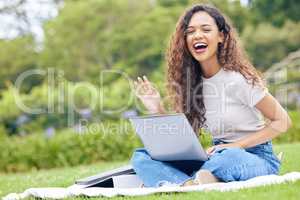 One young hispanic woman working on her laptop while sitting outside on an open field. A beautiful mixed race female student smiling while using her computer to study online on her university campus