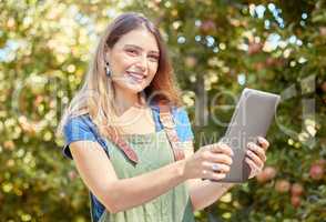 A female apple farmer standing and using a digital tablet while checking her plants. Smiling woman using technology to prepare for harvest on her farm. Monitoring plant growth and agriculture