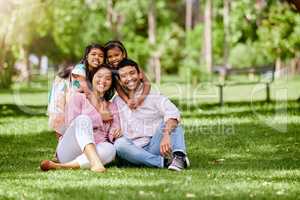 Portrait of happy asian family in the park. Adorable little girls bonding and hugging their parents outside in a park. Full length husband and wife sitting and enjoying free time with their daughters