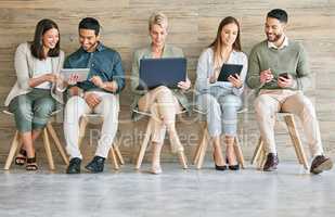 Business could not exist without technology. Full length shot of a diverse group of businesspeople sitting in a row together and using technology.