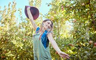 Excited young woman jumping for joy in an apple orchard on a sunny day outside. Happy and cheerful farmer feeling optimistic, free and full of energy after a fruitful harvest on her successful farm