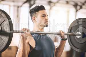 Focused bodybuilder lifting heavy weights. Active athlete building arm muscle with a heavy barbell. Strong trainer doing his workout routine in the gym. Muscular fit man in the gym