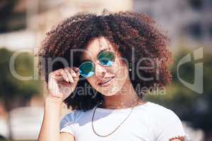 Cool, happy hispanic woman wearing sunglasses outside. Cheerful young woman with a curly afro wearing trendy, stylish sunglasses while enjoying a summer day at the park outside. Young woman smiling