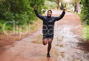 Young hispanic fit male athlete cheering with his fists in the air while on a run in a forest in the rain outside in nature. Exercise is good for health and wellbeing. Happy to reach his fitness goals