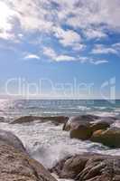 Waves crashing against rocks in the ocean under a blue cloudy sky with copy space. Scenic landscape of boulders or big stones in the sea at a popular summer location in Cape Town, South Africa