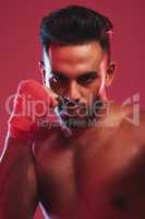 Portrait of one fit and strong handsome mixed race kickboxer isolated against a red studio background and getting ready to fight. Hispanic man posing shirtless in a punching stance. Focused on target