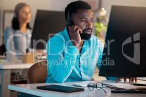 One young african american call centre telemarketing agent talking on a headset while working on a computer in an office. Focused businessman consultant operating a helpdesk for customer service support