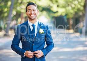 Handsome groom wearing a blue suit with a white shirt and tie. Bridegroom fastening his jacket while standing outdoors on a sunny day