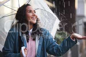 I like to feel the raindrops. a young woman holding her hand out to feel the rain in the city.