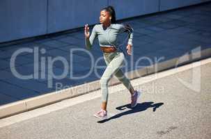 Fit and active African American woman listening to music through earphones and running alone in the city. Black woman focused on fitness and speed while jogging and wearing her phone in an arm holder