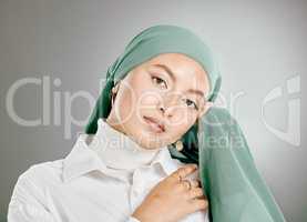 Studio portrait of beautiful muslim woman isolated against a grey background. Young woman wearing hijab or headscarf showing traditional arab modesty holding her hands together and looking at camera
