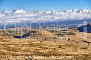 Volcano crater with copy space on a cloudy horizon. High angle view of an empty barren nature scene of desert grass fields over a mountain in Mauna Loa, Hawaii. Undisturbed hills for hiking adventure