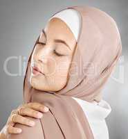 Closeup of a beautiful muslim woman isolated against grey studio background. Young woman with smooth skin wearing a hijab or headscarf, showing her natural looking eyelash extensions and jewellery