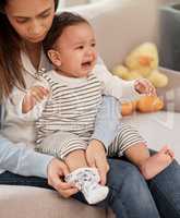 Id rather be barefoot. a young baby girl crying while her mother changes her clothes at home.