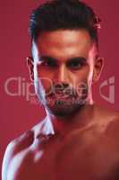 Closeup portrait of one fit and strong handsome mixed race man isolated against a red background in a studio and posing shirtless. Headshot of serious and focused hispanic man looking determined