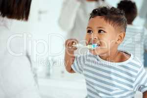 Look mom, I got every tooth. an adorable little boy brushing his teeth while his mother helps him at home.