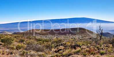 Landscape of dry land and blue sky with copy space. A dormant volcano in an open uncultivated location. Nature scenery of bushy vegetation on mountain summit of a volcanic land in Big Island, Hawaii