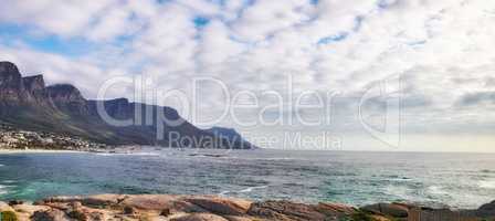 Beautiful view of the ocean and mountains in Cape Town. Water, waves and rocky planes along the coast. Cloudy sky on top of the beauty of the oceans divine essence of nature in the Western Cape.