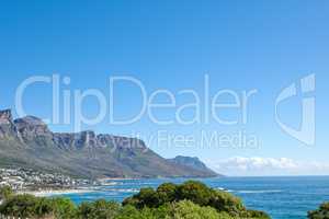 Costal city surrounded by nature with an iconic landmark in the background in urban Cape Town. Scenic view of mountain with vibrant green plants near a calm ocean and a blue sky day with copy space.