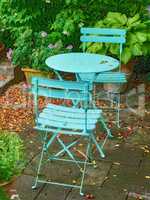 Blue courtyard metal chairs and table in serene, peaceful, lush, private backyard at home on a summers day. Patio furniture set and seating in empty and tranquil garden with fresh flowers and plants