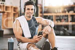 Portrait of happy trainer in the gym. Strong, fit man listening to music after a workout. Strong bodybuilder taking a break from exercise class. Smartphones and music are needed when training