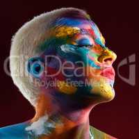 We live in a rainbow of chaos. Studio shot of a young woman posing with multi-coloured paint on her face.