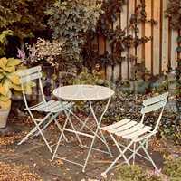 Courtyard metal chairs and table in a serene, peaceful, lush, private backyard at home in autumn. Patio furniture set in outdoor space, seating in an empty and tranquil garden with scrub plants