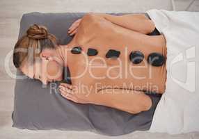 Time to melt away tension and ease muscle stiffness. High angle shot of a mature woman enjoying a relaxing hot stone massage at a spa.