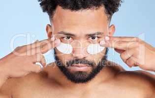 Fighting wrinkles one treatment at a time. Studio portrait of a handsome young man wearing under eye patches against a blue background.