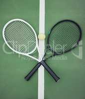 Above view of two tennis rackets and a ball on an empty court in a sports club. Aerial view of black and white tennis gear and equipment on asphalt. Ready to play a competitive game versus an opponent