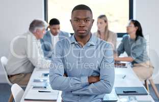 I will not be stopped. Portrait of a confident young businessman standing with his arms crossed in an office while his colleagues have a meeting in the background.