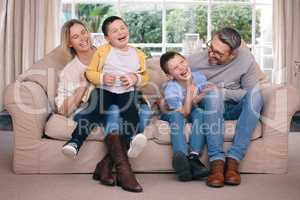 Tickling is one mans pleasure. a young family happily bonding together on the sofa at home.