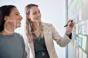 The worlds ready. two businesswomen brainstorming with sticky notes on a chalkboard.