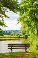 Park bench overlooking the view by the lake in the countryside. Scenic view of trees and greenery by a river with an empty public bench in summer. Landscape view of an idyllic natural environment