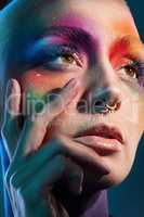Born to stick out. Studio shot of a young woman posing with multi-coloured paint on her face.