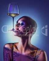 Im a goddess thats as fine as wine. Studio shot of an attractive young woman wearing edgy makeup and holding a glass of wine in her mouth against a blue background.