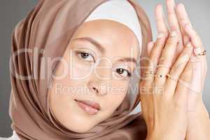 Studio portrait of beautiful muslim woman wearing a brown headscarf and showing multiple rings on her hands. Female wearing hijab and glowing makeup with trendy jewelry showing off her modest beauty