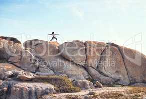 Awaken the warrior within you. a young woman practicing yoga on a boulder.